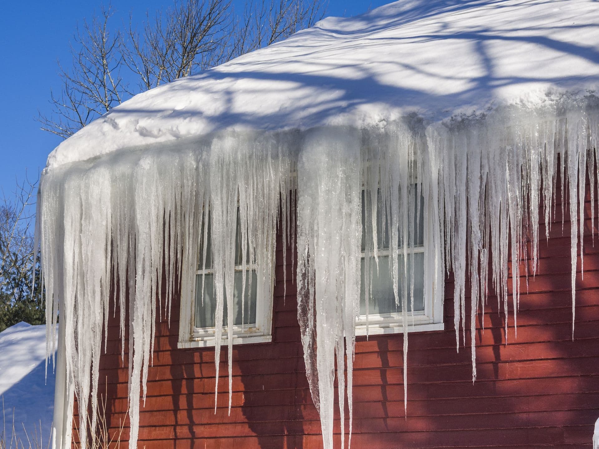 Large icicles hang from a roof on a red house.