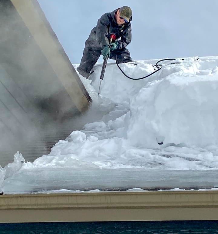 A worker removes an ice dam from a roof covered in snow and ice.