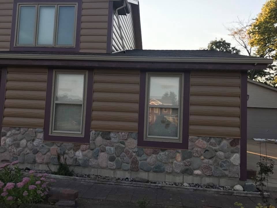 Aluminum clad wood frame windows with brown trim on a brown house with log cabin-like siding and stone foundation.